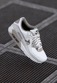 Nike Air Max 90 sneaker featuring a white and beige colorway, leather and mesh materials, textured accents, and a visible air cushioning unit.