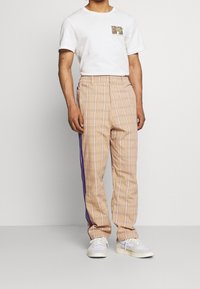 Harmaat kuviolliset housut, joissa on violetit sivuvaihteet, rento istuvuus ja joustava vyötärö. Yhdistetty yksinkertaiseen valkoiseen T-paitaan.