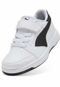 Baskets en cuir blanc avec des accents noirs, présentant une pointe arrondie, des perforations pour la ventilation, et une sangle Velcro avec des lacets.