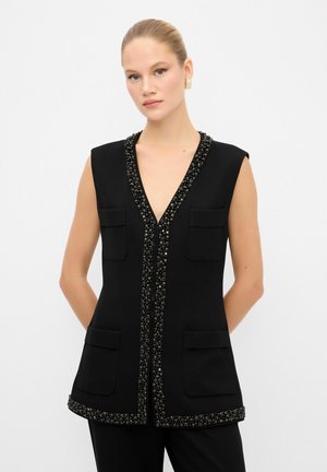 Gilet nero senza maniche con scollatura a V profonda, impreziosito da un bordo decorativo di perline lungo il collo e l'orlo, con tasche anteriori.