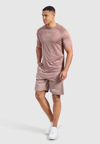 Camisa deportiva de manga corta en rosa claro con un logo sutil y pantalones cortos a juego; ambos confeccionados con una suave tela que absorbe la humedad.