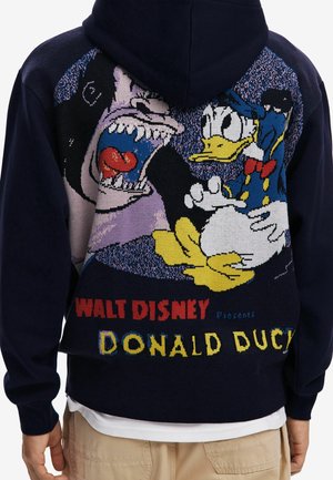 Námořnická mikina s velkým pleteným motivem Donalda Ducka reagujícího na řvoucího vlka, s textem "Walt Disney představuje Donalda Ducka" ve spodní části.