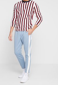 Gestreiftes Langarmhemd in Rot, Weiß und Marineblau. Hellblaue Jogginghosen mit weißen Seitenstreifen. Weiße Turnschuhe vervollständigen das Outfit.