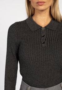 Donkergrijze ribgebreide sweater met een kraag en drie zwarte knoopaccenten. Het materiaal lijkt zacht met een aansluitende pasvorm.