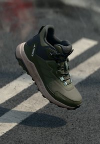 Chaussure de randonnée vert olive avec une surface texturée, accents noirs et lacets réfléchissants. Dispose d'une semelle rembourrée et d'une semelle extérieure robuste.