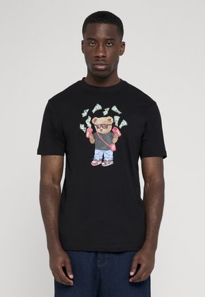 Mand iført sort t-shirt med grafik af en bjørn, der holder lyserøde pengesække og omgivet af svævende dollarsedler.