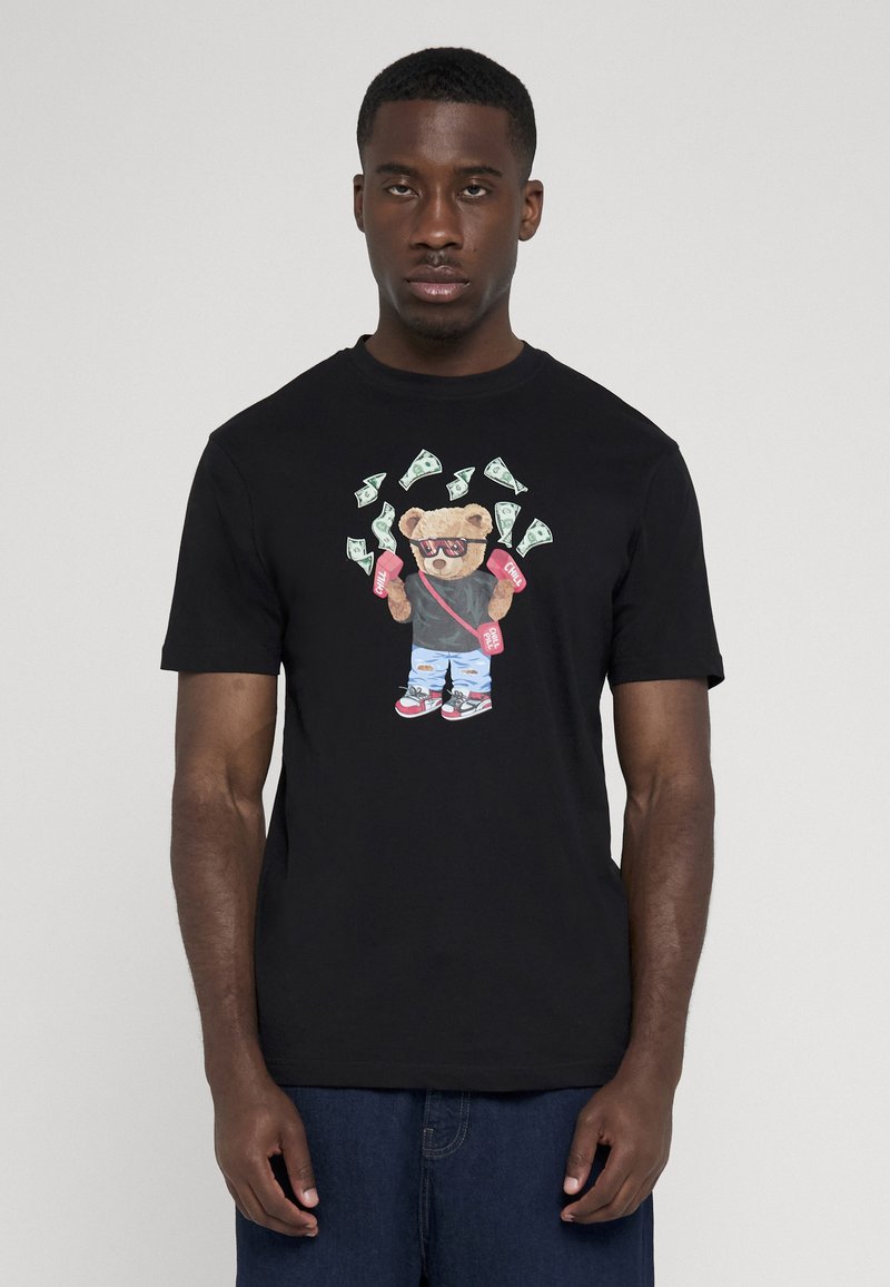 Homme portant un t-shirt noir avec un graphisme d’ours tenant des sacs roses d’argent et entouré de billets de dollar flottants.
