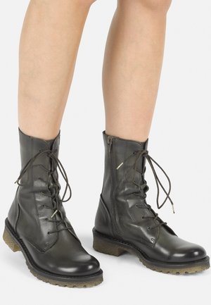 Botas negras de cuero con cordones, con una suela de goma texturizada, altura hasta el tobillo y cierre de cremallera lateral; cuentan con costuras destacadas y cordones.