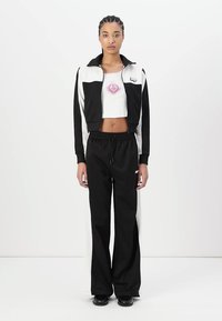 Veste zippée noir et blanc avec un design court, associée à un pantalon large noir. Comprend un graphique de cœur coloré sur le haut blanc.
