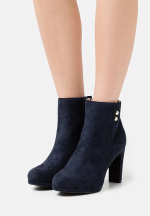 Granatowe botki z miękkiego zamszu, z zaokrąglonym noskiem, obcasem typu klockowego o wysokości 4 cali oraz złotymi guzikami po bokach.