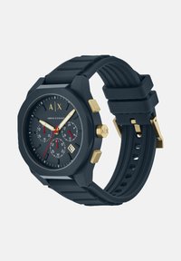 Armani Exchange sat s tamnom plavom silikon trakastom remenu, okruglim brojčanikom, zlatnim akcentima i dvostrukim hronografskim brojčanicima. Ima izražene oznake sati.