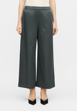 Nő magas derekú, széles szárú sötétszürke, felhajtott szegélyű rövid nadrágban, fekete hegyes orrú magassarkúval párosítva.