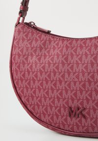 Sac à main à motifs rouges avec une forme incurvée, fermeture éclair et logo embossé. Fabriqué à partir de matériaux durables avec une finition texturée.
