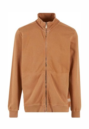 Kihúzható dzseki rozsdaszínben, magas gallérral, bordás mandzsettával és két elülső zsebbel. Puha, texturált anyagból készült.