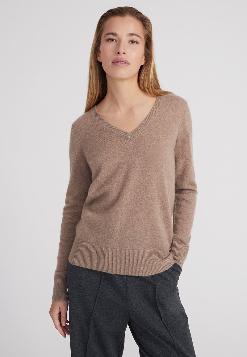 V-Ausschnitt-Pullover aus weichem beigem Kaschmirgemisch. Rippbündchen und Saum, lockere Passform und subtile Textur sorgen für visuelles Interesse.