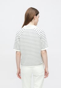 Fehér rövid ujjú pólóing tengerészkék vízszintes csíkokkal, klasszikus gallérral és laza szabással, hátulról ábrázolva.