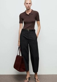 Polo shirt a coste marrone, pantaloni neri a vita alta e borsa a tracolla in suede bordeaux. Cintura nera con fibbia dorata. Sandali neri con cinturini.
