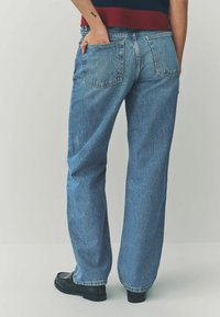 Jeans in denim blu chiaro con design a gamba dritta, dotati di due tasche posteriori e una texture consumata. Abbinati a mocassini neri.