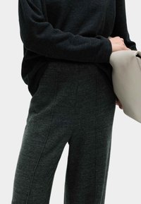 Szary, fakturowany sweter dzianinowy z długim rękawem, połączony z ciemnoszarymi, szerokimi spodniami z delikatnymi szwami. Modelka trzyma jasną torebkę.