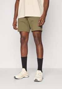 Pantaloni scurți din bumbac de culoare verde măslin, cu o croială dreaptă, asortați cu șosete negre și adidași bej. Tricou simplu de o culoare neutră.