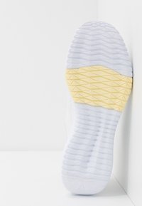 Bílá podrážka tenisky s texturovaným gumovým povrchem a žlutým akcentem, s geometrickým vzorem pro trakci a stabilitu.