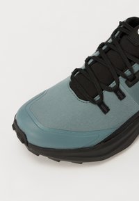 Lichtblauwe sport schoen met zwarte accenten, voorzien van een textuurstof bovenwerk, gebogen ontwerp en zwarte veters. Rubberen zool voor grip.
