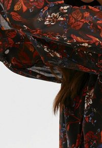 Genomskinlig blus med lång ärm, prydd med ett blommönster i rött, vitt och blått på en svart bakgrund. Lätt och flödande tyg.