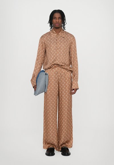 Chemise à motifs marron et pantalon en tissu lisse, présentant des motifs de croissant, accompagnés d'une pochette pliante bleu clair. Chaussures noires.