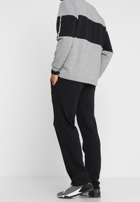 Grå sweatshirt med svart horisontell rand, svarta joggers och grå sneakers. Tyget ser mjukt ut; elastiska muddar och benslut är synliga.