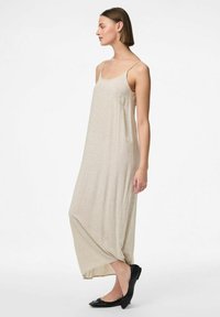 Robe maxi beige avec des fines bretelles, réalisée en tissu texturé, présentant une coupe ample et un ourlet incurvé, associée à des ballerines noires.