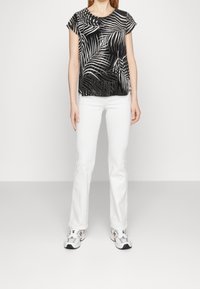 Top negro de manga corta con diseño de hojas en blanco, hecho de una tela ligera. Combinado con jeans blancos acampanados y zapatillas.