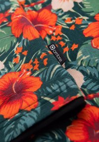 Blommönstrad textil med röda hibiskusar och gröna blad på en mörk bakgrund; inkluderar en liten "ombre"-etikett på kanten.