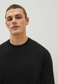 T-shirt nera in cotone con maniche corte e colletto girocollo, texture liscia, design minimalista, senza motivi o accenti visibili.