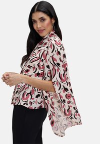 Tryckt blus i lätt tyg med ett mönster av rosa, svart och vitt blommigt, hög halsringning och flödande kappa-lika ärmar.