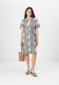 Napapaita musta-valkoinen ruudullinen mekko, jossa on kukkakuviota. Lyhyet hihat, vyötäröltä vyötetty, polvimittainen helma. Yhdistetty sandaalien kanssa.