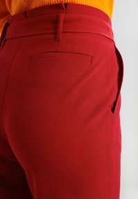 Röda byxor i slätt tyg med en figursydd design, fickor utan lock och rak benpassform. Midjan är väldefinierad.