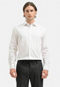 Vit långärmad skjorta med knappar, slim fit, mjukt tyg, klassisk krage, framplacket med knappar, bärs med svarta byxor.