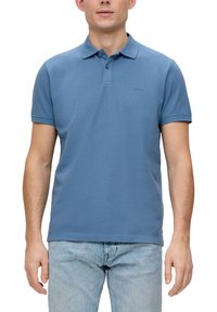 Modrá bavlnená polo košeľa s klasickým golierom, krátkymi rukávmi a dvojitým zapínaním na gombíky. Jemný logom na hrudi. Nosená s svetlými džínsami.