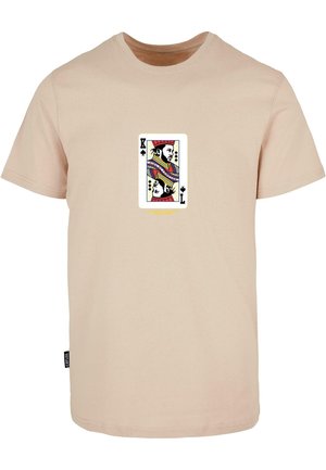 Beżowa koszulka z krótkim rękawem z umieszczoną na środku grafiką króla pik oraz czarną boczną metką z napisem „CAVALER”.