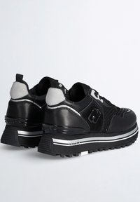 Par de zapatillas gruesas negras y grises con lados texturizados, suelas gruesas y con tracción, y tiradores en los talones sobre un fondo liso.