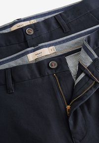 Dva páry námornícky modrých slim fit nohavíc s viditeľnými gombíkmi, zipsami, pútkami na opasok a pruhovanými vnútornými štítkami na páse so značkou "NEXT".