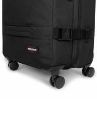 Maleta negra con ruedas, fabricada con tela resistente. Cuenta con un parche con la marca, una correa ajustable y ruedas suaves y redondeadas para facilitar su movilidad.