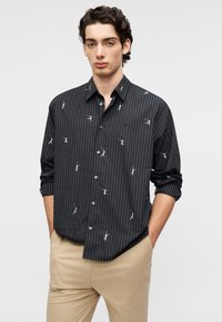 Chemise à rayures noires avec motifs de danseurs ludiques, design à boutons, manches longues et texture de tissu lisse. Détail d'ourlet plissé.