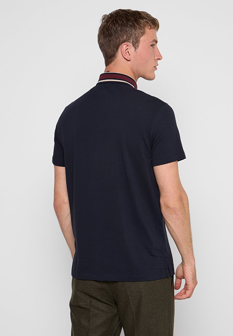 Marineblauwe polo met korte mouwen en een contrasterende kraag met rode en witte strepen. Gemaakt van een gladde katoenmix. Klassieke pasvorm.