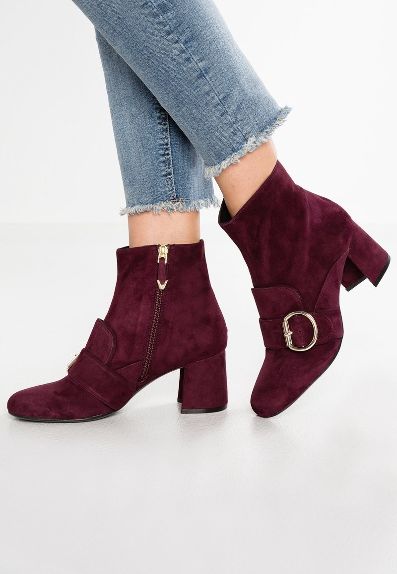 Burgundy mockakskinn ankle boots med rund tå, blockklack, dragkedja på sidan och en dekorativ spännsnobb på remmen. Fransade jeans synliga.