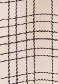 Gros plan sur un tissu beige avec un motif en grille noire formé de lignes torsadées créant des formes carrées.