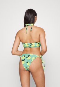 Conjunto de biquíni com design de decote halter, base verde menta e padrões de folhas pretas contrastantes. Ties no pescoço e nos lados. Textura suave.