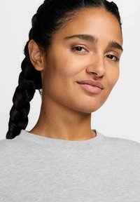 Sudadera gris claro con cuello redondo. La tela parece suave con una textura sutil. Se puede ver un peinado trenzado que muestra el tono de piel natural.