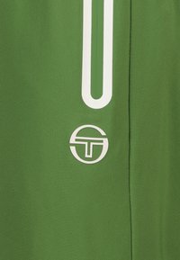 Grüne Sportshorts mit einer glatten Textur, versehen mit einem weißen vertikalen Streifen und einem runden Logo in einem kontrastierenden Design.
