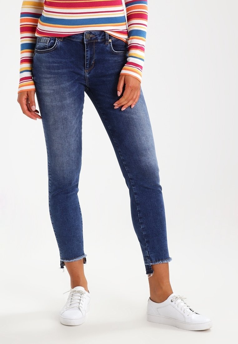 Skinny jeans in donkerblauwe denim met een vervaagde afwerking, voorzien van een mid-rise taille, vijf-pocket ontwerp en rafelige zoom. Gecombineerd met witte sneakers.